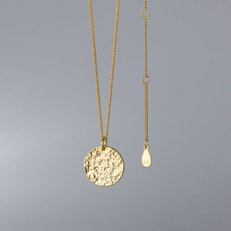 Gold necklace with a round pendant on a gray background