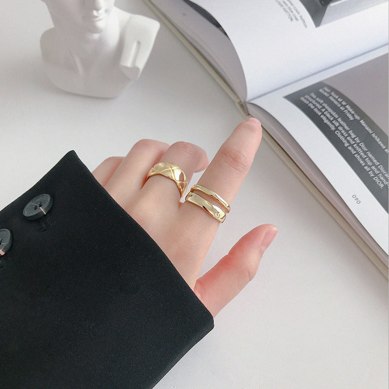Hand wearing two gold rings with a blurred book in the background