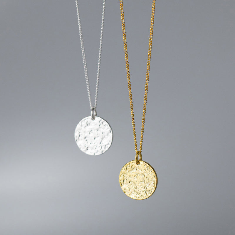 Two necklaces with round pendants, one gold and one silver, on a gray background.