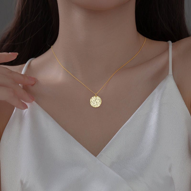 Gold necklace with a round pendant on a model wearing a white top.