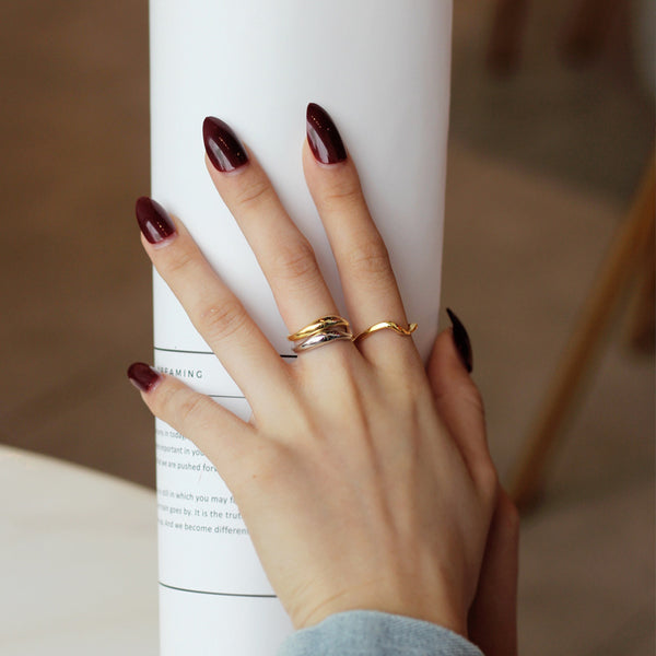 Hand with maroon nail polish and gold rings on a blurred background