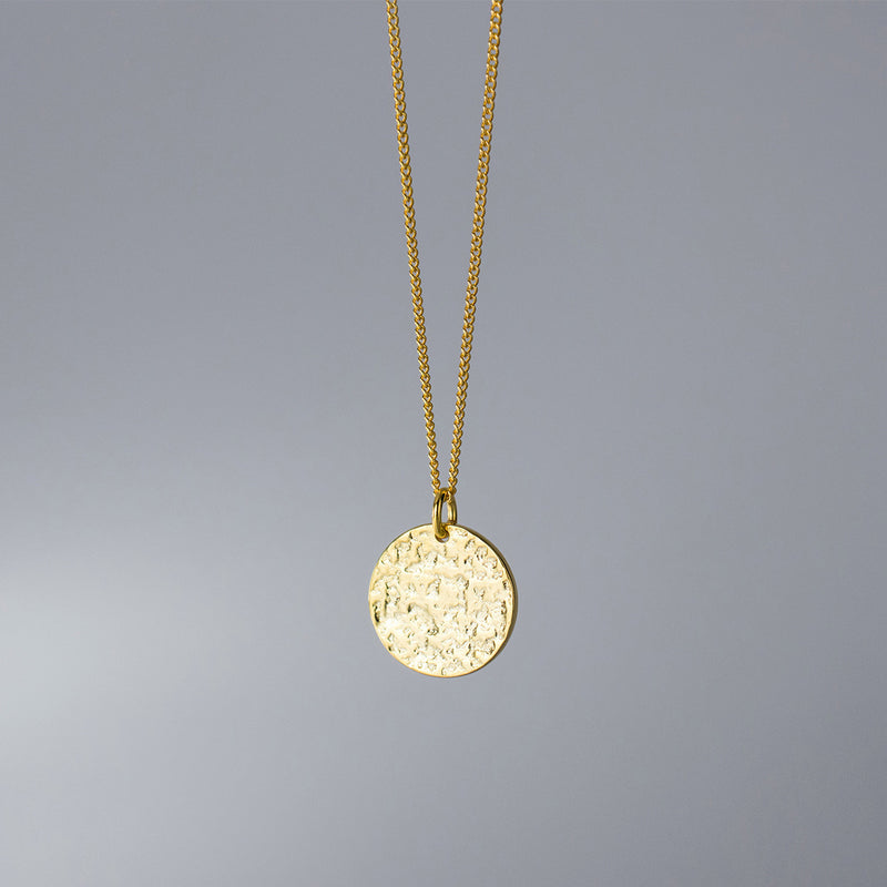 Gold necklace with a round pendant on a gray background
