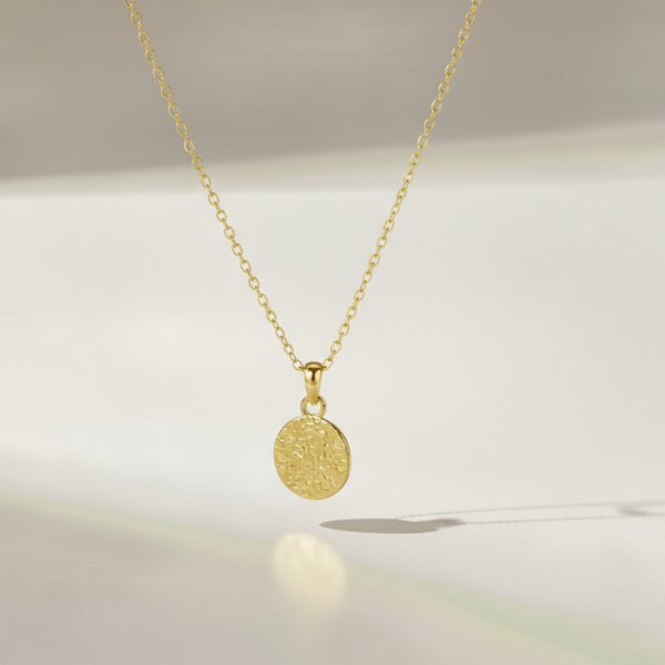 Gold necklace with a round pendant on a soft white background