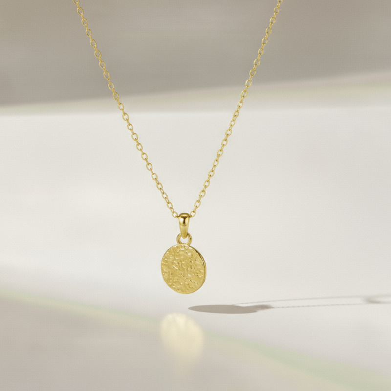 Gold necklace with a round pendant on a soft white background