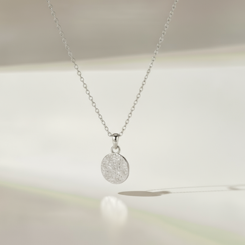 Silver necklace with a round pendant on a soft white background