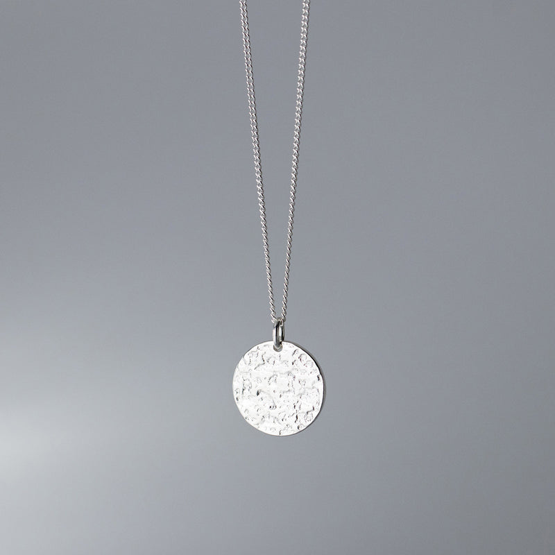 Silver necklace with a round pendant on a gray background